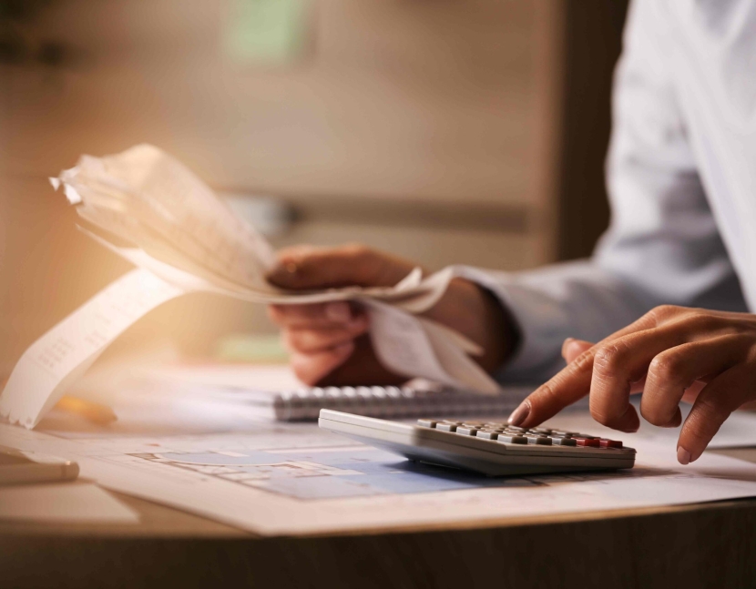 Close-up of economist using calculator while going through bills and taxes in the office.